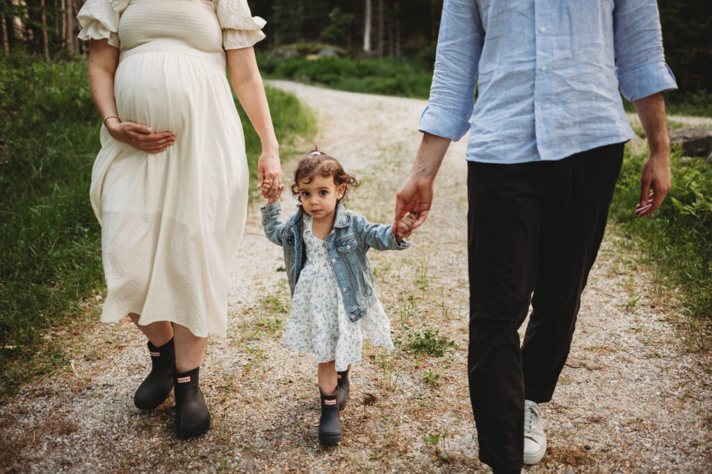 Blue Hill maternity photographer capturing family along wooded path by cottage