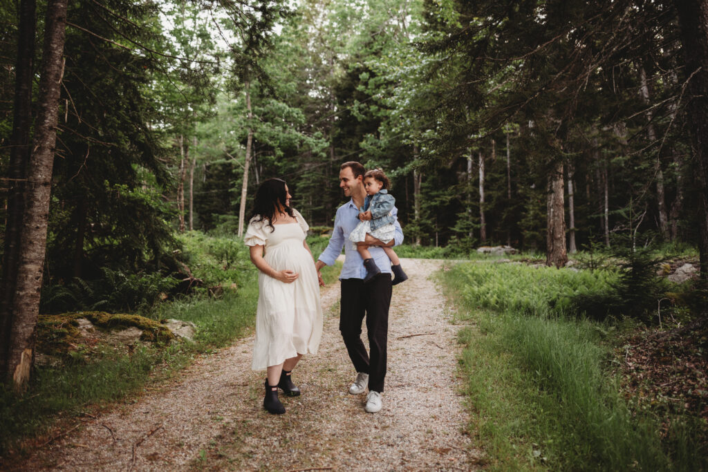 Blue Hill maternity photographer capturing family along wooded path by cottage